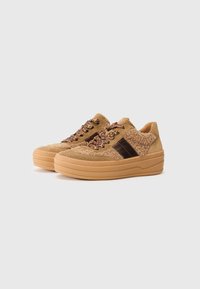 Tan suede sneakers with a textured upper, featuring a brown leather side stripe and patterned laces, set on a chunky tan sole.