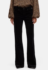 Pantaloni a zampa in velluto a coste nero con tasche frontali e una leggera lucentezza, abbinati a una camicetta a maniche lunghe con stampa leopardata e maniche a palloncino.