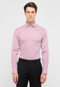 Camicia a righe rosse e bianche a maniche lunghe con colletto appuntito, dal design aderente, abbinata a pantaloni neri a contrasto.