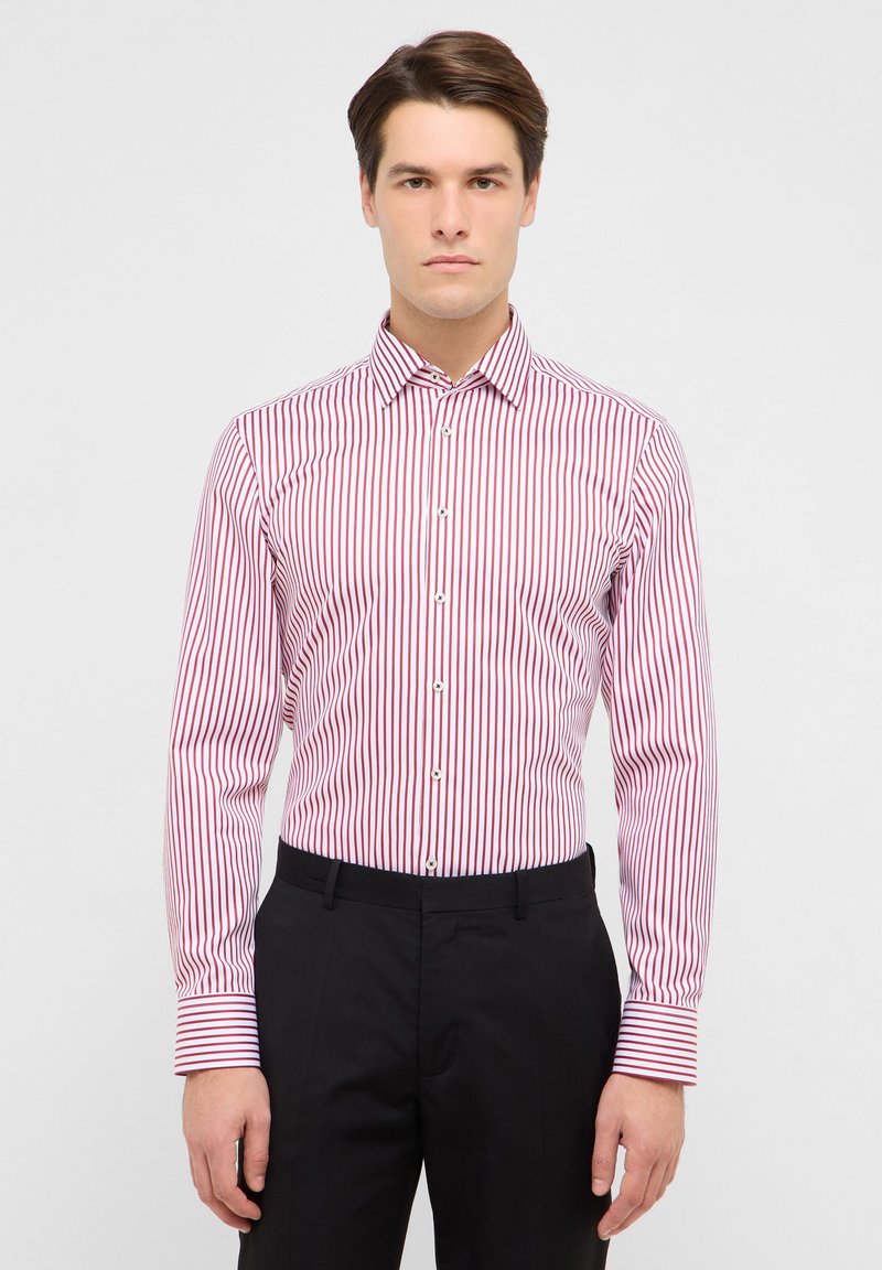 Camicia a righe rosse e bianche a maniche lunghe con colletto appuntito, dal design aderente, abbinata a pantaloni neri a contrasto.