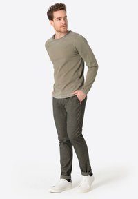 Olivgrünes Langarmhemd mit rundem Ausschnitt, kombiniert mit dunkel gemusterten Hosen und weißen Sneakers, mit hochgekrempelten Ärmel.