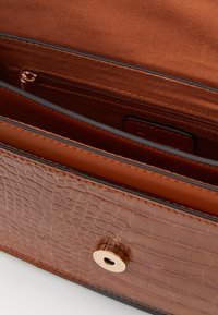 Ruskea teksturoitu nahkabagin sisus, jossa on vetoketjullinen tasku ja magneettinen napsautussuljin. Suora vuoraus ja erottuvat yksityiskohdat näkyvissä.