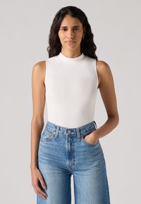 White sleeveless bodysuit with a high neckline, paired with high-waisted light blue denim jeans. Smooth texture, fitted design.