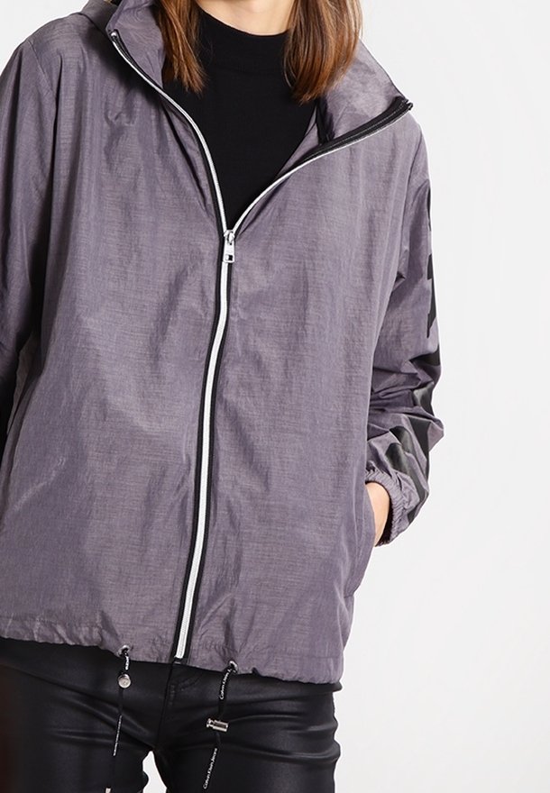 Szara, lekka kurtka z zamkiem błyskawicznym, elastycznymi mankietami i sznurkami przy dolnym brzegu; gładka faktura o subtelnym połysku.