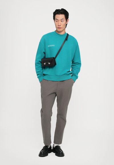 Turkis sweatshirt med rund hals, grå tapered bukser, og sort crossbody taske med sølv hardware, båret med sorte sko.