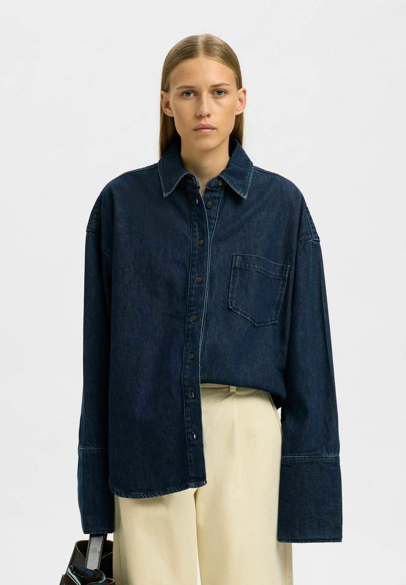 Dunkelblaues Denim-Hemd mit Knopfleiste, großem Kragen und übergroßen Ärmeln. Verfügt über eine einzelne Tasche auf der linken Brust.