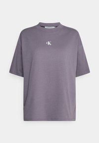 Camiseta de algodón gris de gran tamaño con cuello redondo y mangas cortas, que presenta un pequeño logo blanco "ck" en el pecho. Textura suave.