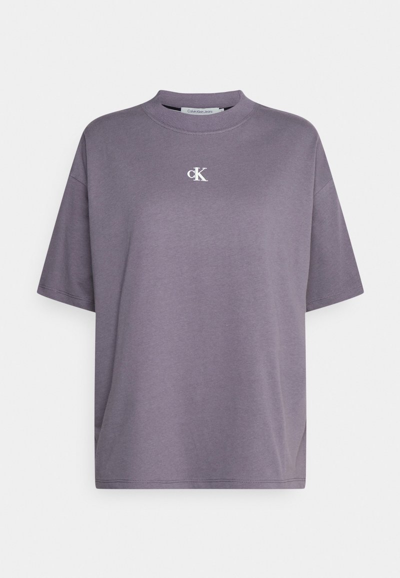 Camiseta de algodón gris de gran tamaño con cuello redondo y mangas cortas, que presenta un pequeño logo blanco "ck" en el pecho. Textura suave.