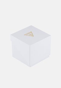 Weißer würfelförmiger Karton mit goldenem Guess-Logo in der Mitte oben, vor einem schlichten hellen Hintergrund.
