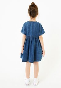 Robe en denim à manches courtes, décolleté rond, taille froncée et jupe évasée. Sa couleur est un bleu moyen avec une finition en denim texturé.