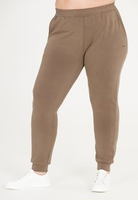 Bruna joggerbyxor i mjukt tyg med smal passform, elastisk midja, sidofickor och ribbade manschetter, tillsammans med vita sneakers.