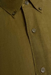 Close-up of olive green button-up shirt showing collar, placket, and four buttons with visible stitching on fabric.
