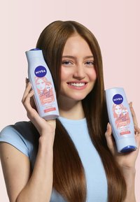 NIVEA-Shampoo-Flaschen in hellblau mit dunkelblauen Akzenten, ausgestattet mit pinken Etiketten. Die Modells hält zwei Flaschen und hat lange, gerade braune Haare.