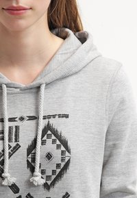 Sudadera con capucha gris que presenta una capucha con cordón, tela texturizada y patrones geométricos negros en la parte delantera.