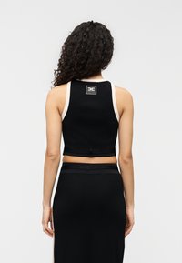 Μαύρο κοντό τοπάκι με αντίθετοι μπεζ ιμάντες. Διαθέτει τετράγωνο λογότυπο στην πλάτη και εφαρμοστή σχεδίαση. Λεπτή υφή υφάσματος.