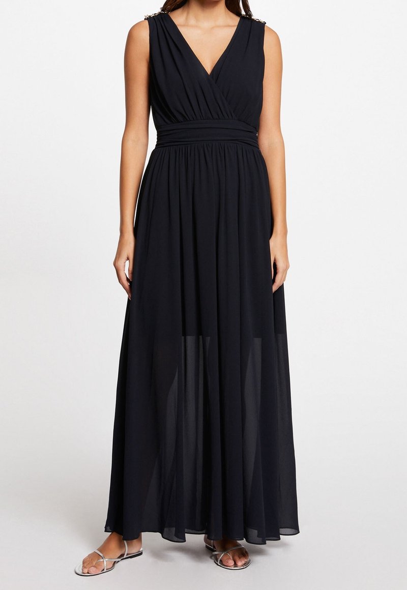 Robe maxi noire avec un décolleté en V, taille froncée et superposition drapée. Présente des accents en bijoux sur les épaules et une texture fluide et transparente.