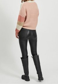 Neulepaita, jossa on vaaleanpunaisia, kermaisia ja kultaisia raitoja, yhdistetty mustiin keinonahkahousuihin ja polven korkeisiin mustiin saappaisiin.