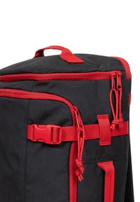 Czarny plecak z czerwonymi zamkami, paskami i elementami metalowymi. Posiada górny uchwyt i kilka przegród. Wykonany z trwałego materiału o teksturowanym wykończeniu.