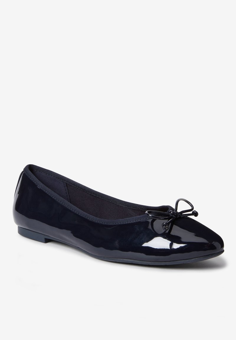 Chaussure plate de ballet noire brillante avec bout arrondi et petit nœud décoratif sur le dessus, semelle plate et bord élastique autour de l’ouverture.