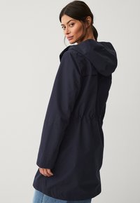 Marineblauwe waterdichte parka met een capuchon, elastische taille en lange mouwen. Kenmerkt zich door een soepele textuur en subtiele stikseldetails.