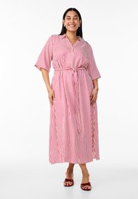 Vestido de botonadura en rojo y blanco a rayas, con mangas cortas y cintura atada. Hecho de una tela de textura suave, que llega a medio pantorrilla.