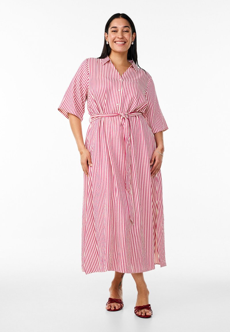 Vestido de botonadura en rojo y blanco a rayas, con mangas cortas y cintura atada. Hecho de una tela de textura suave, que llega a medio pantorrilla.