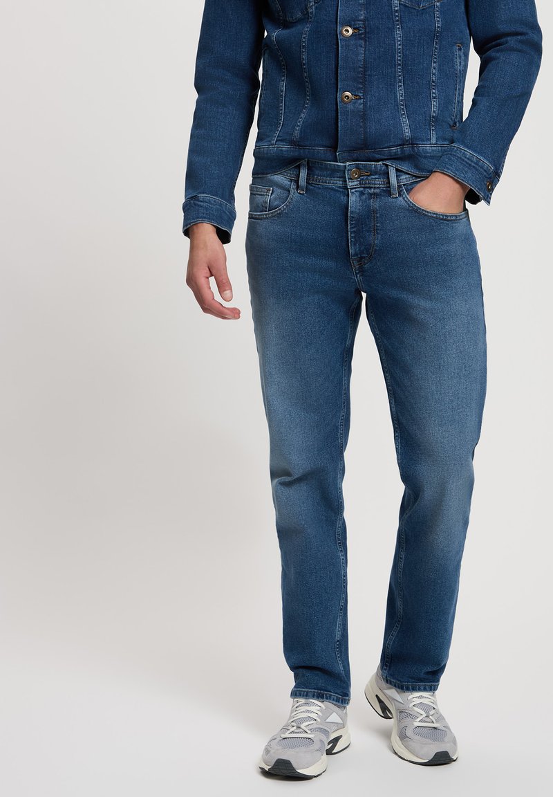 Jeansowa kurtka i dżinsy w średnim niebieskim odcieniu. Kurtka ma metalowe guziki i dwie przednie kieszenie. Dżinsy mają klasyczny krój i miękką teksturę.