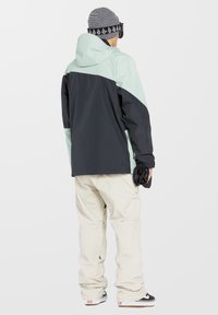Chaqueta con capucha en verde menta claro y negro, acompañada de pantalones holgados en crema. Cuenta con cierre de cremallera, puños ajustables y un corte atlético moderno.