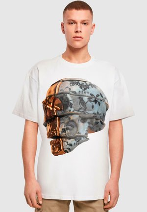 Hvid t-shirt med et stort grafisk motiv af et kranium, dekoreret med sorte florale mønstre og gyldne detaljer, med distinkte 3D-lag.