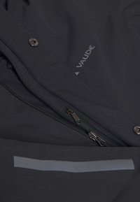 Giacca nera realizzata in un tessuto liscio e testurizzato, con tasca con zip, chiusura a scatto e logo stampato. Presenza di un accento riflettente sottile.