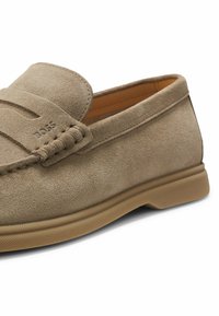 Mocassin beige en daim pour homme avec logo embossé, détails cousus et semelle en caoutchouc, vu de profil.