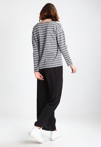 Grauer und weiß gestreifter Langarmoberteil, lockere Passform, kombiniert mit schwarzen weit geschnittenen Hosen und weißen Sneakers. Weicher Stoff, lässiges Design.
