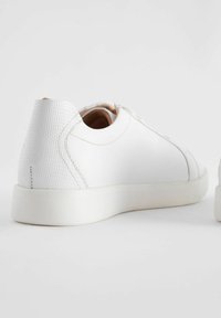 Baskets blanches en cuir lisse, avec un talon texturé, une forme arrondie et une semelle en caoutchouc à profil bas. Design minimaliste avec des coutures ton sur ton.