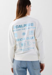 Witte sweatshirt met blauwe graphics en tekst op de achterkant, inclusief logo's, patronen en de zin "BEACH CLUB." Casual pasvorm met geribbelde boorden.