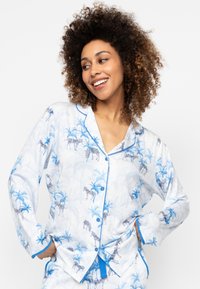 Witte pyjama set met blauwe zebra- en palmbomenprints, met een kraag, knoopsluiting aan de voorkant en contrasterende blauwe afwerking op de mouwen.