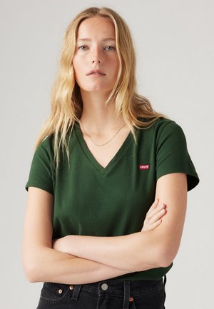 V-neck green cotton t-shirt with short sleeves and a small red Levi's logo on the left chest. Model wears black high-waisted jeans.