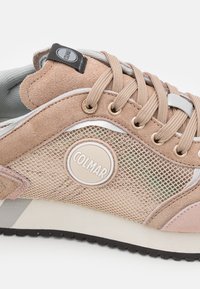 Béžové suedové a síťované tenisky s hnědými tkaničkami, kruhovým logem a stříbrnými akcenty. Mají texturovanou podešev pro lepší přilnavost.