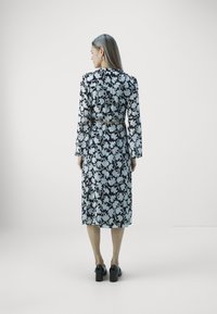 Kleid mit einem schwarz-weißen Blumenmuster, langen Ärmeln, einem taillierten Bund und einer Länge bis zur Mitte der Wade. Glattes Material mit einem fließenden Design.