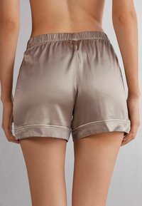 Pantalones cortos de satén en un color beis degradado, con una cinturilla fruncida, dobladillos enrollados y un delicado ribete blanco en los puños.