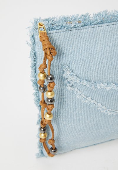 Lichtblauwe denim tas met franjes, voorzien van een bruine leren schouderband versierd met metalen kralen in goud, zilver en zwart.