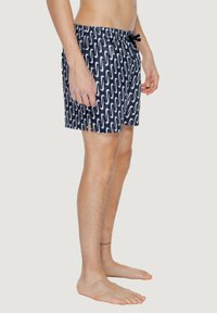 Costumi da bagno da uomo in blu navy con un motivo a onde bianche. Realizzati in tessuto leggero e ad asciugatura rapida, con vita elastica e cordino.
