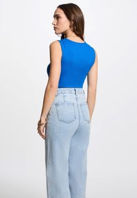 Blauwe geribbeerde tanktop gecombineerd met lichtblauwe high-waisted jeans. De top heeft een getailleerde pasvorm, terwijl de jeans een relaxte pasvorm en zakken hebben.