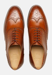 Scarpe da dress in pelle marrone con dettagli brogue, allacciatura chiusa, punta liscia e una silhouette elegante con una forma leggermente arrotondata.