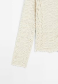 Pull à texture crème avec un design froncé, manches longues et ourlet en forme de vague. Fabriqué dans un tissu doux et extensible.