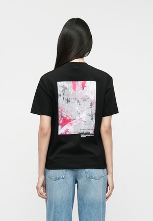 Fekete pamut póló, melynek hátoldalán egy nagy absztrakt grafika található szürkében és rózsaszínben, az alján "KARL LAGERFELD JEANS" felirattal.
