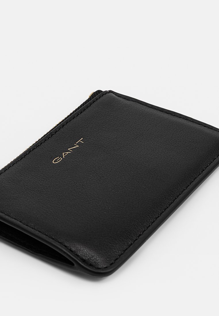 Schwarze Lederbörse mit glatter Textur, Reißverschluss und geprägtem Gold-Logo. Rechteckige Form mit klaren Kanten und minimalistischem Design.