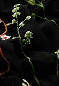 Tissu noir avec des broderies florales complexes en vert, blanc et orange. Présente des détails de points délicats et une surface douce et texturée.