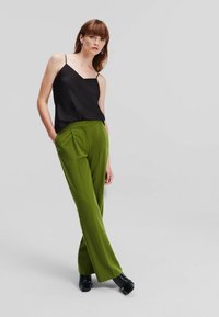 Camasă din satin negru cu bretele subțiri, asociată cu pantaloni verzi, cu talie înaltă și plisați. Modelul poartă pantofi negri cu toc pătrat.