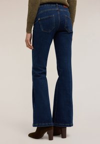 Vaqueros de denim de color azul oscuro con cambio de forma, que presentan una cintura de media altura, dos bolsillos traseros y un dobladillo limpio. Complementados con botas de tacón marrones.