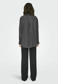 Gray long-sleeve shirt with a back pleat, rounded hem, and buttoned cuffs, paired with black wide-leg pants. Smooth fabric texture.